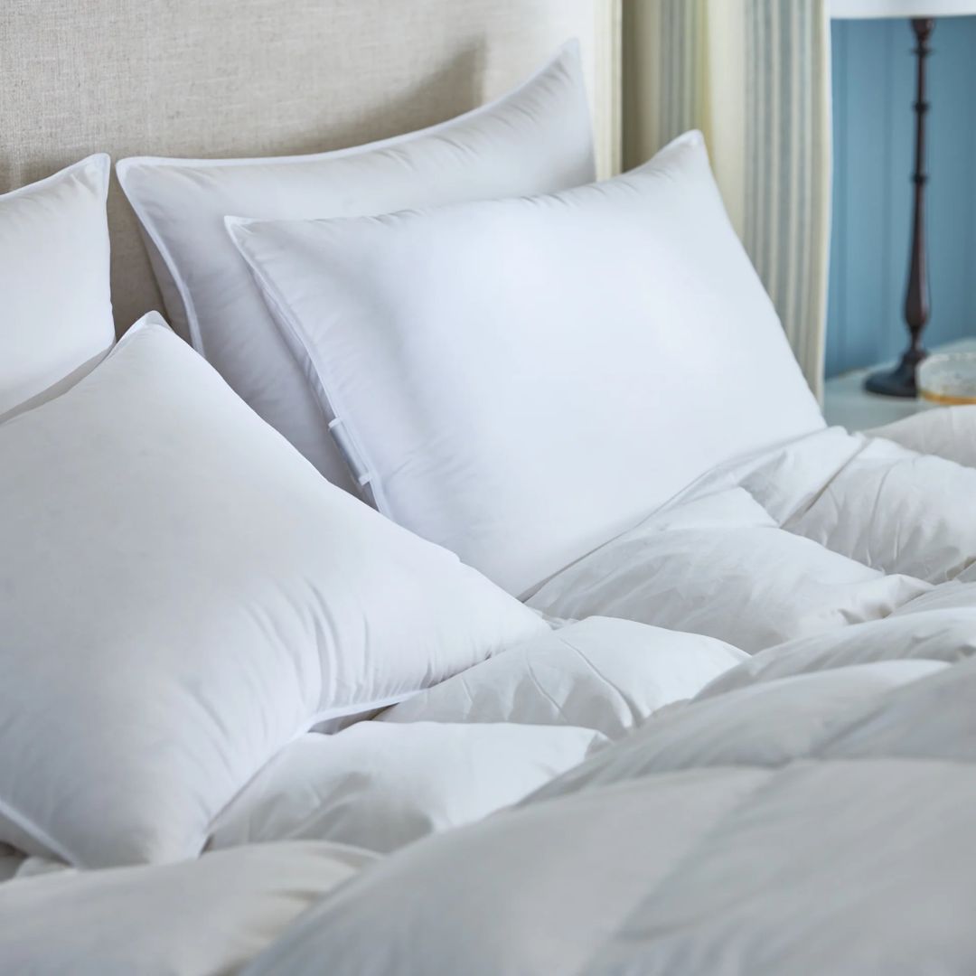 A neatly made bed with a Chamonix pillow and luxury down bedding, beside a beige headboard and lamp on the side table.