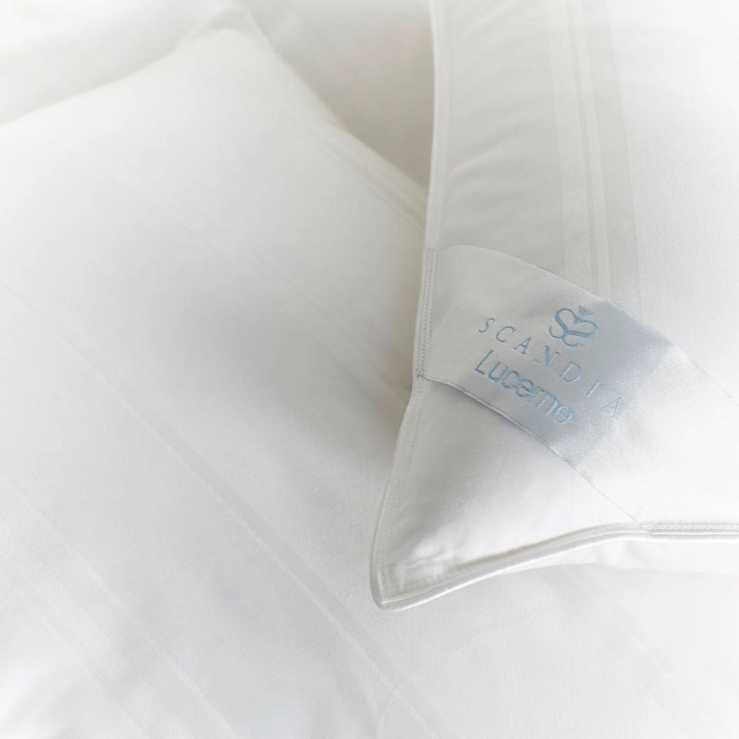 Two Scandia Home pillows, filled with hypoallergenic Hungarian white goose down, arranged on a striped white bed.