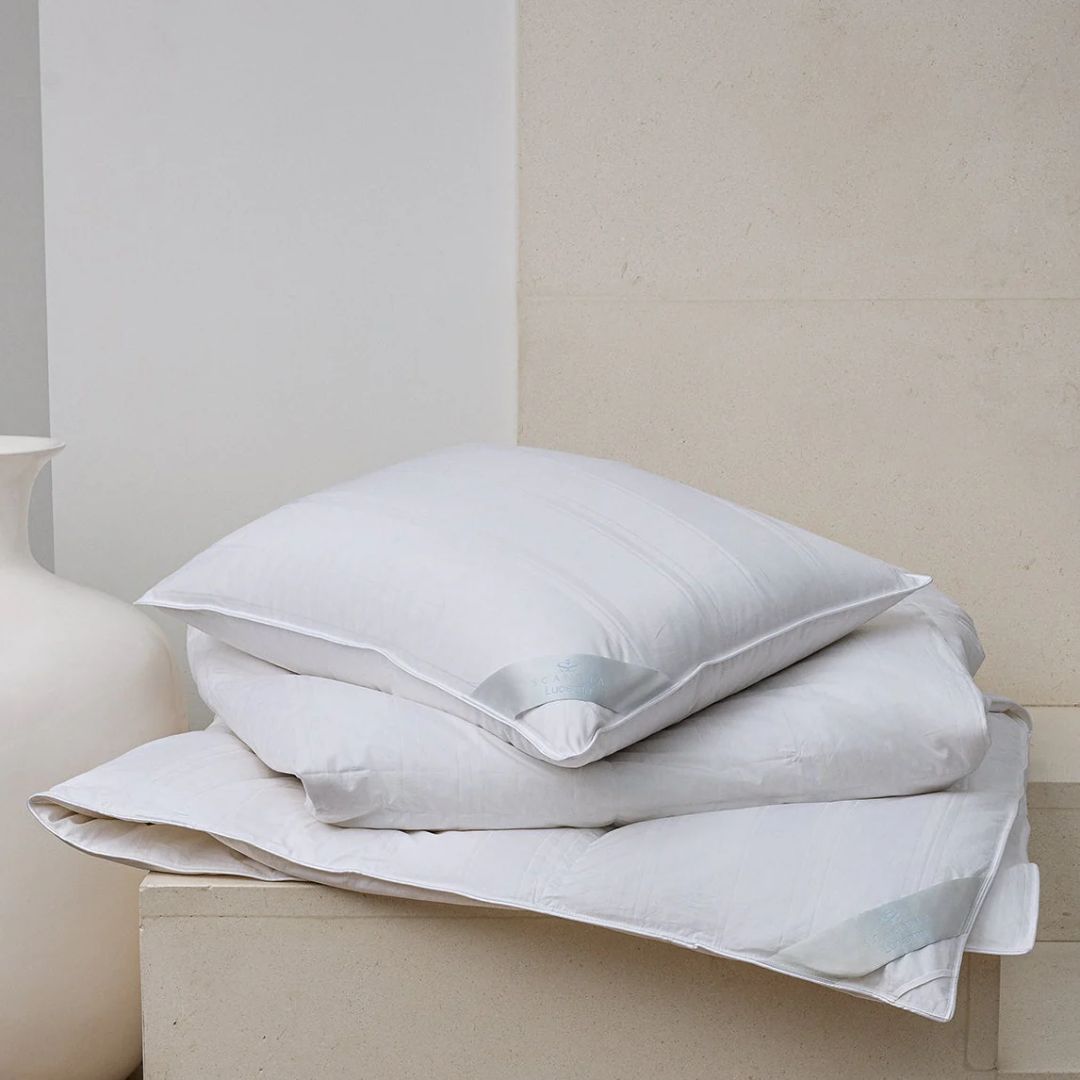 Three hypoallergenic Scandia Home pillows stacked on a stone surface next to a white vase and beige wall.