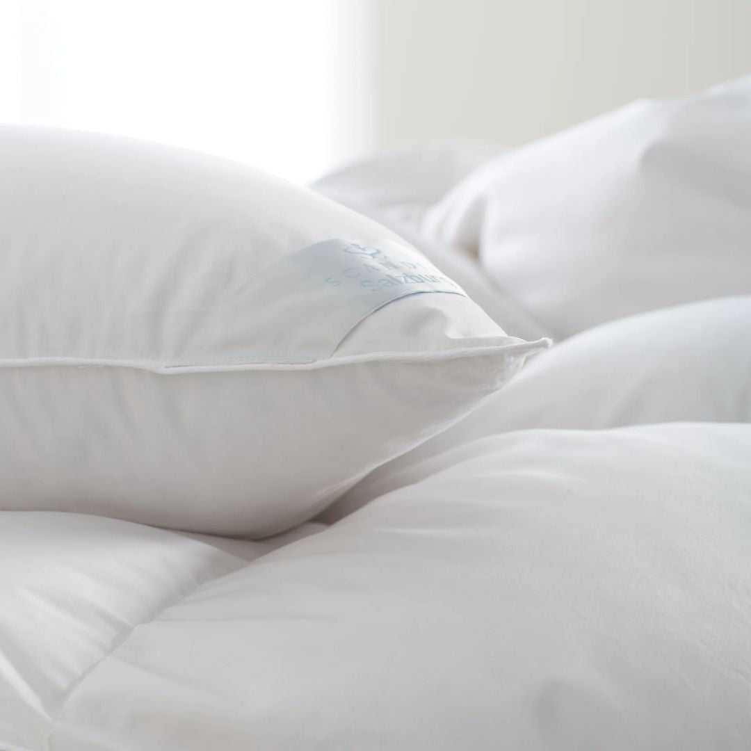 A close-up of Scandia Home pillows stacked on a bed in a softly lit room.