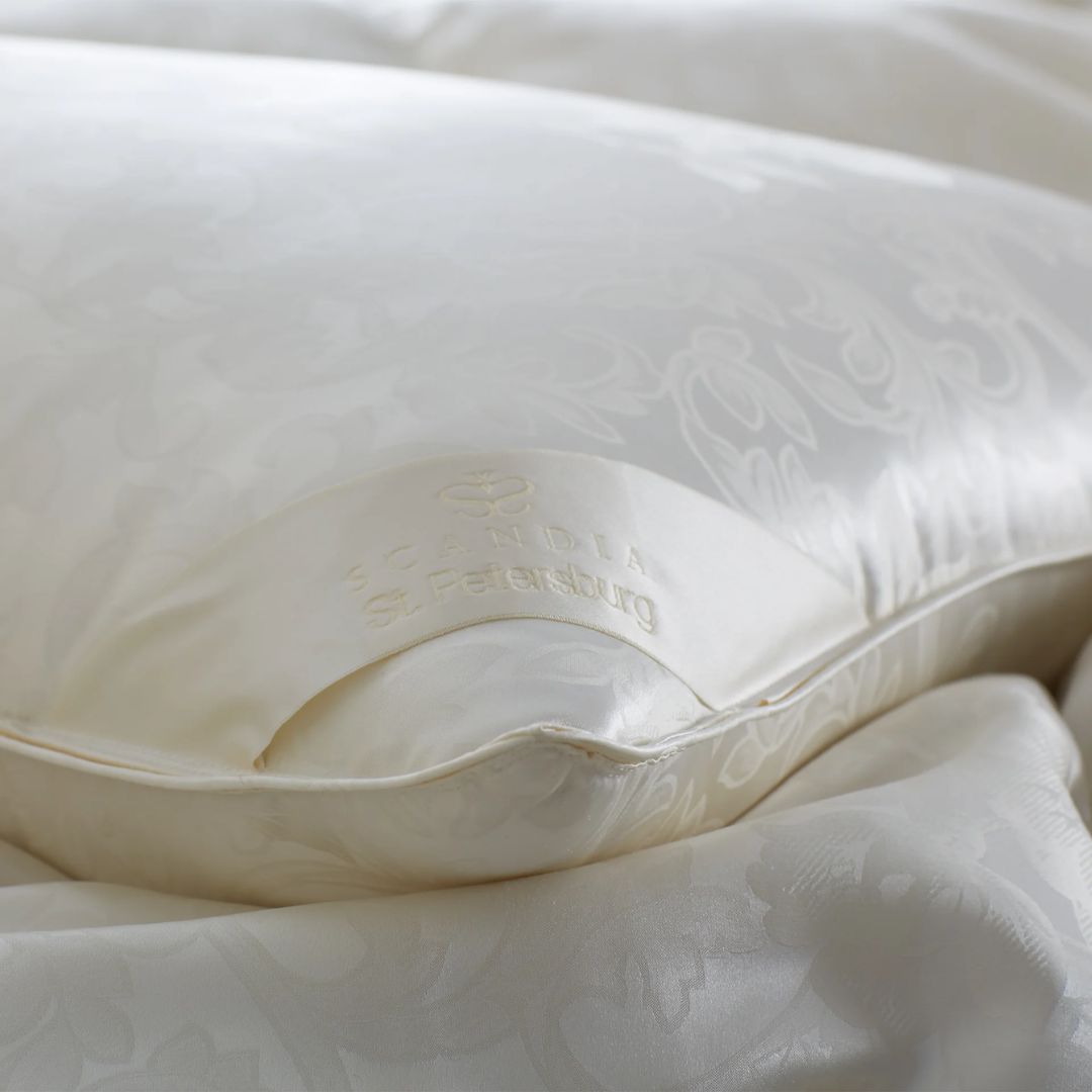 A close-up of a luxury down pillow by Scandia Home, with St. Petersburg embroidery, resting on matching bedding.