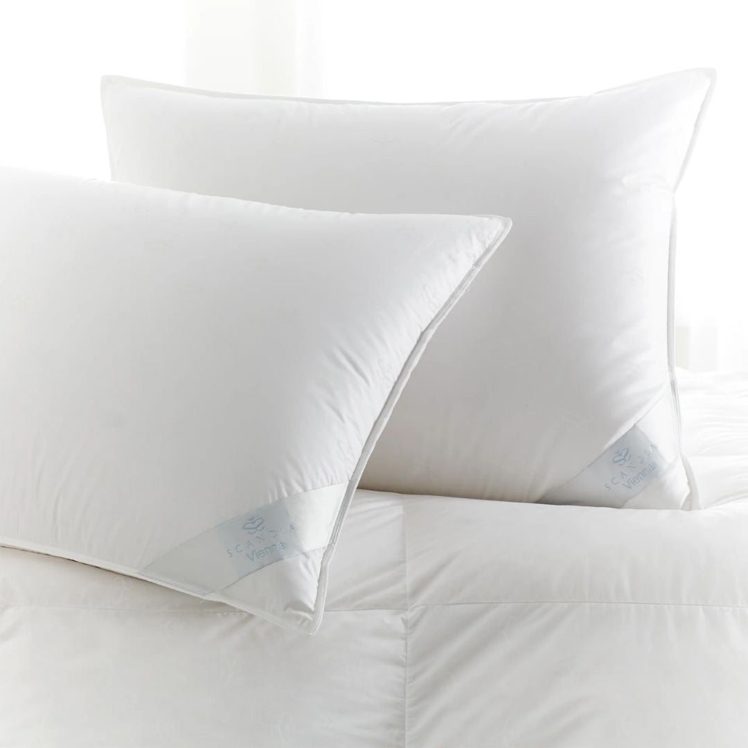 Two white Scandia Home pillows stacked on a white bed with a soft, bright background.