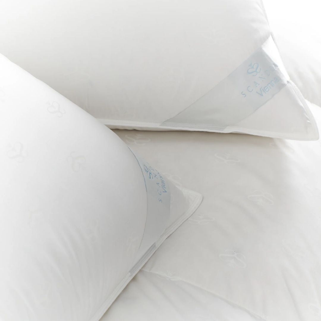Two white luxury down pillows with subtle patterns and light blue tags rest on a white surface.