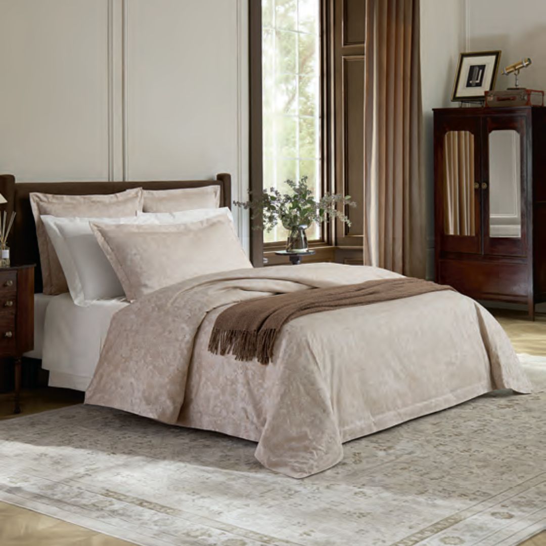 A neatly made bed features a Sferra Altea duvet cover in Italian sateen jacquard, creating an elegant, sunlit bedroom.
