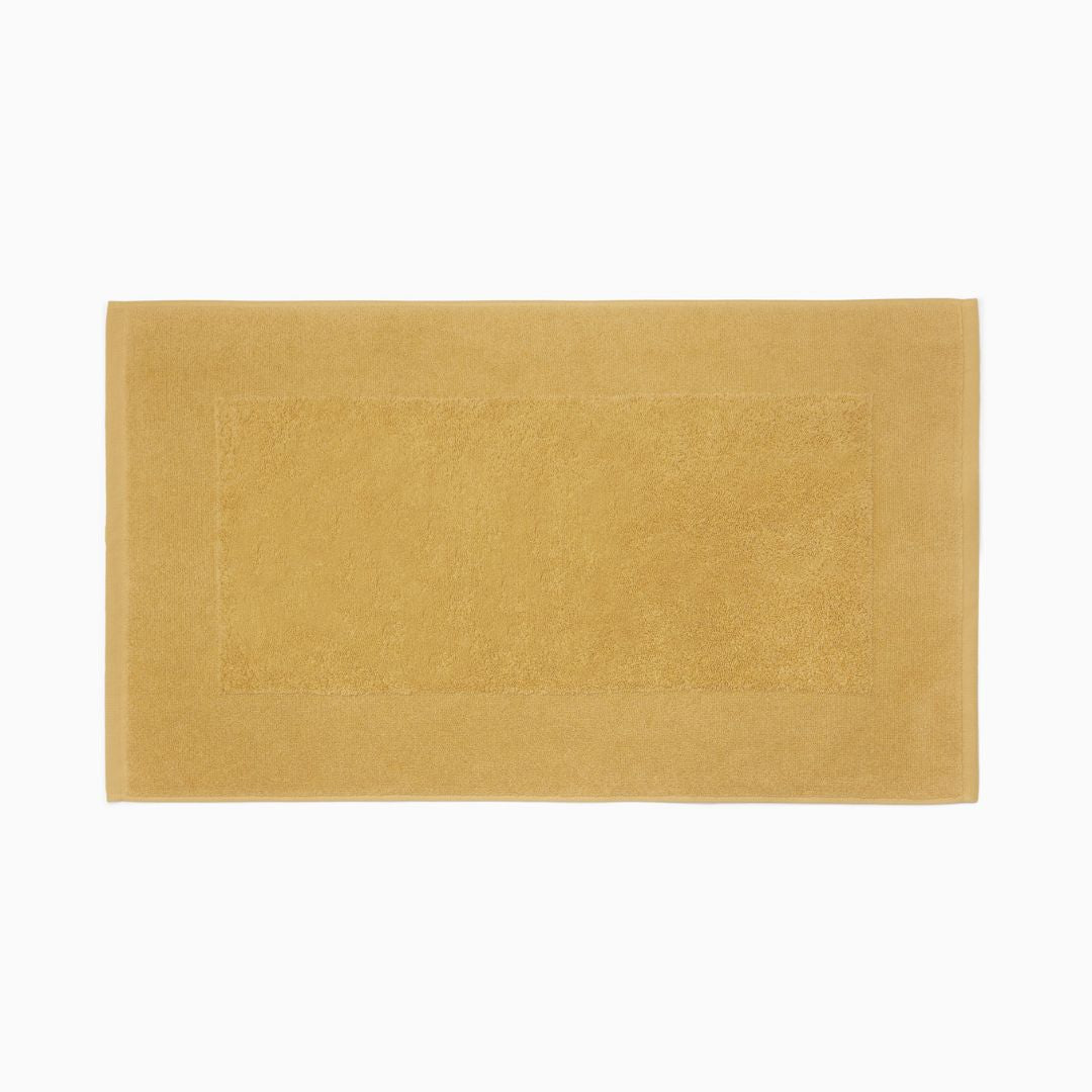 A rectangular mustard yellow bath mat of long-staple combed cotton features a textured center and solid border.