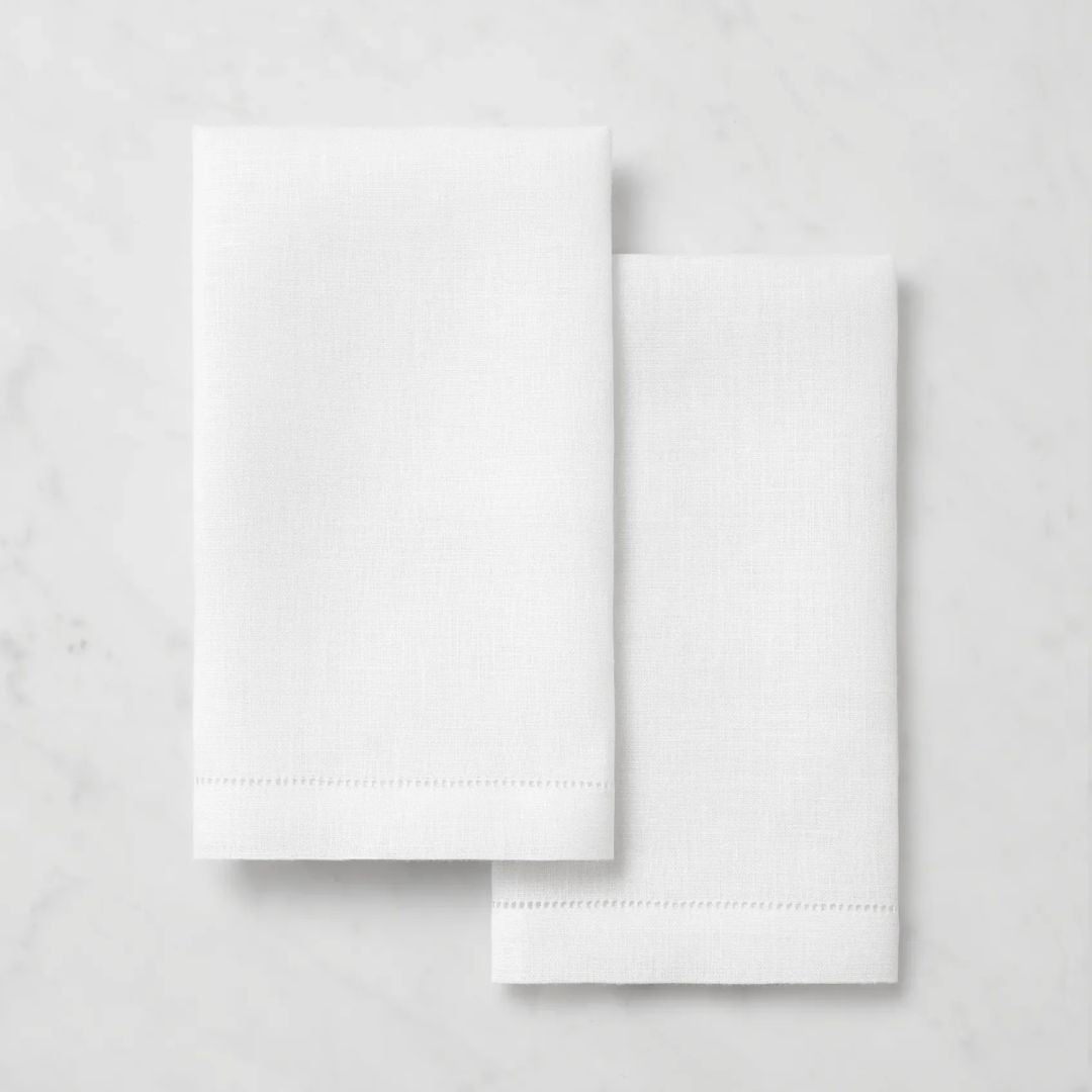 Two neatly folded monogrammed linen towels rest side by side on a light marble surface.