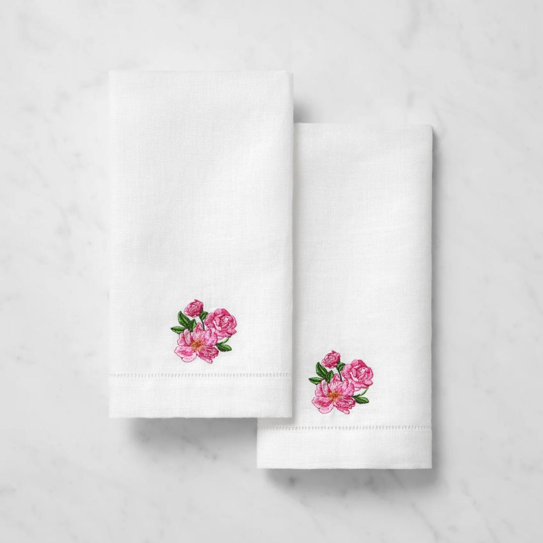 Two white linen guest towels with pink and green embroidered roses, displayed on a white marble surface.