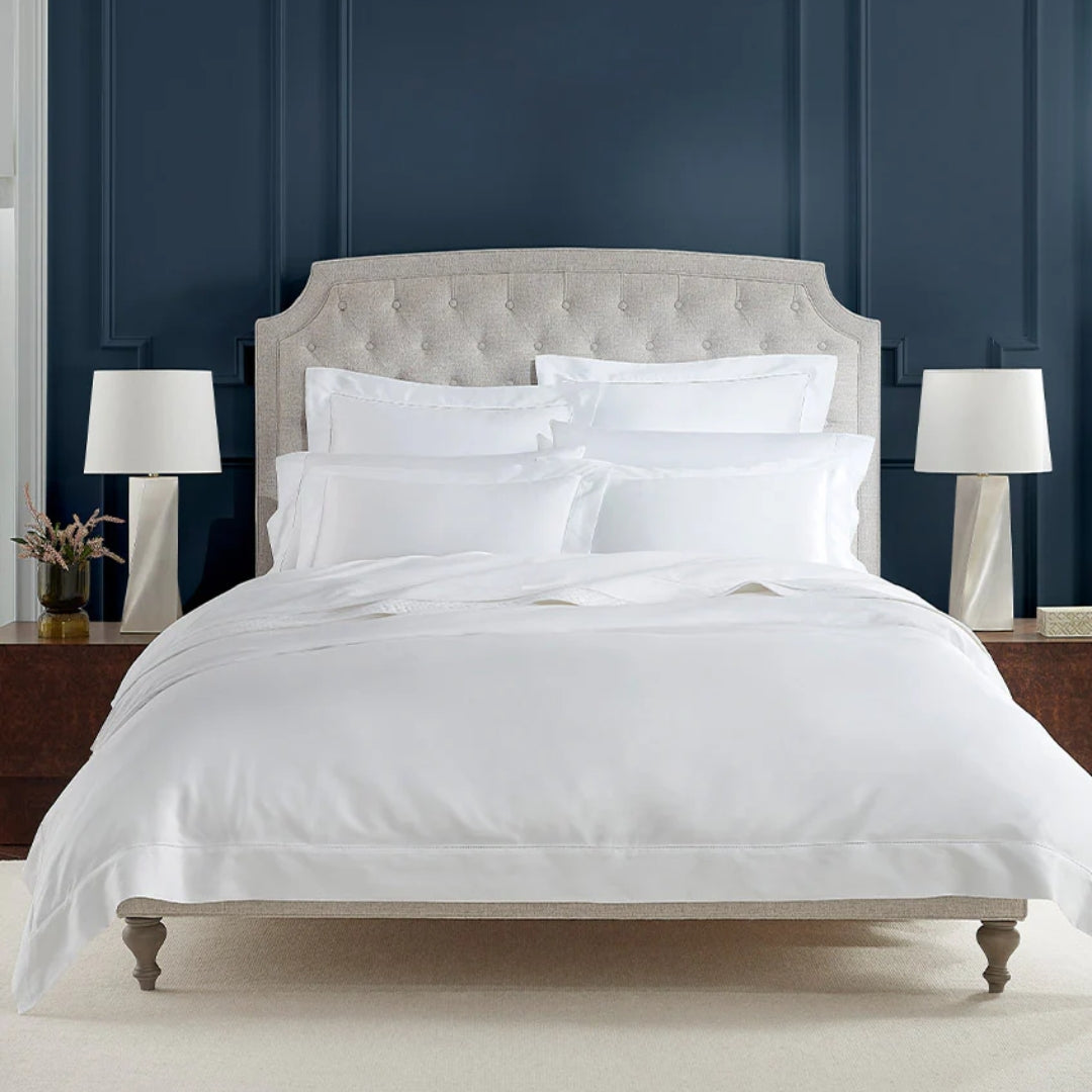 Neatly made bed with white bedding in a bedroom with dark blue walls and white lamps.