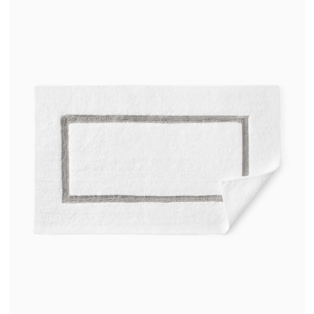A white textured bath towel with a gray stitched rectangular border, shown on a clean white background with one corner folded over.