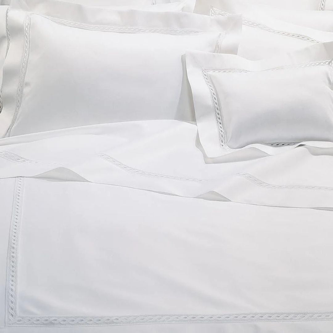 White bed sheets and pillowcases with a lace inset border and subtle decorative details on a neatly made bed.