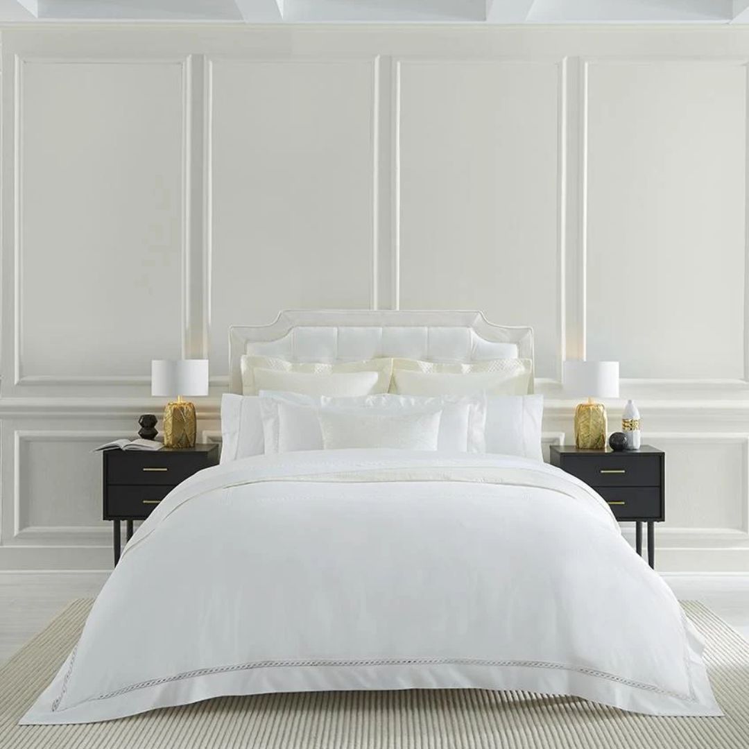 A neatly made bed with luxury bedding is flanked by two black nightstands with lamps and decorative objects.