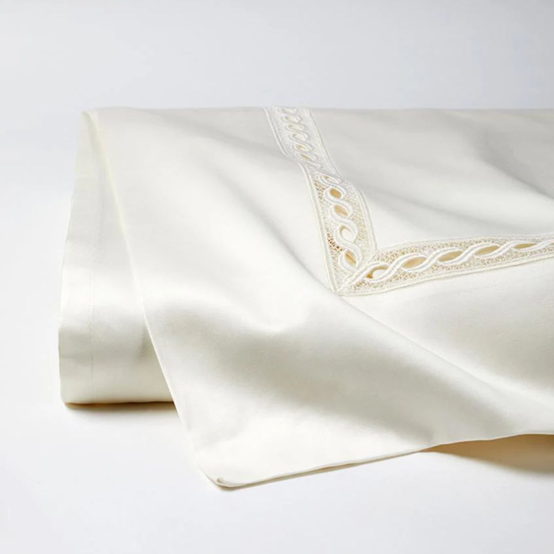 A folded white luxury bed sheet with decorative lace trim, crafted from soft Egyptian cotton sateen on a light background.