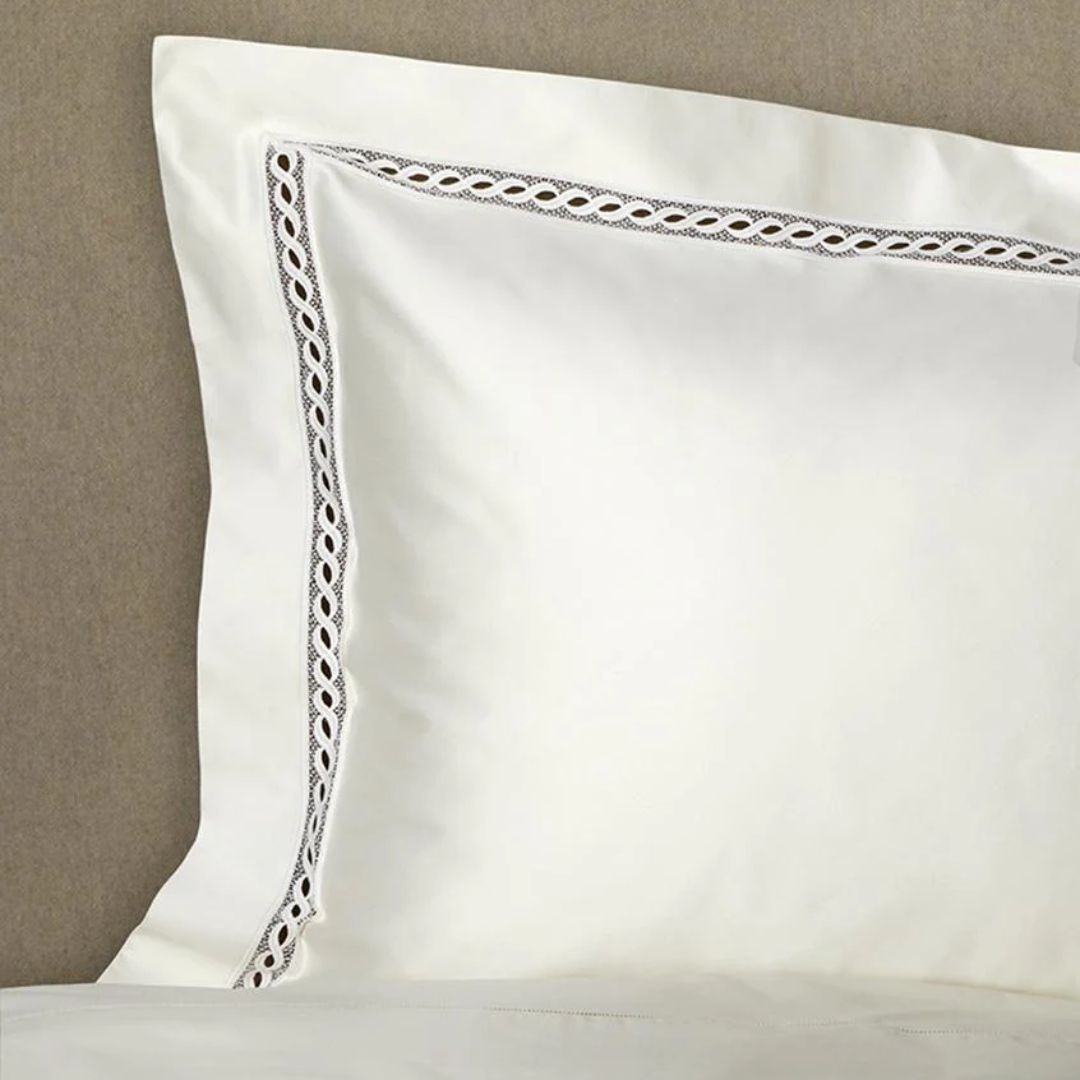 A white pillow with decorative lace rests against a beige headboard, paired with luxury Egyptian cotton sheets.