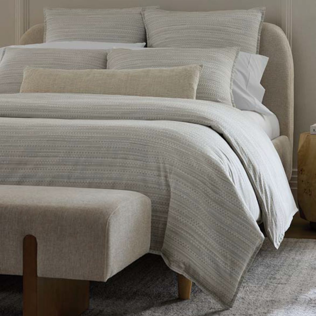 Neatly made bed with striped bedding and pillows in a bedroom setting.