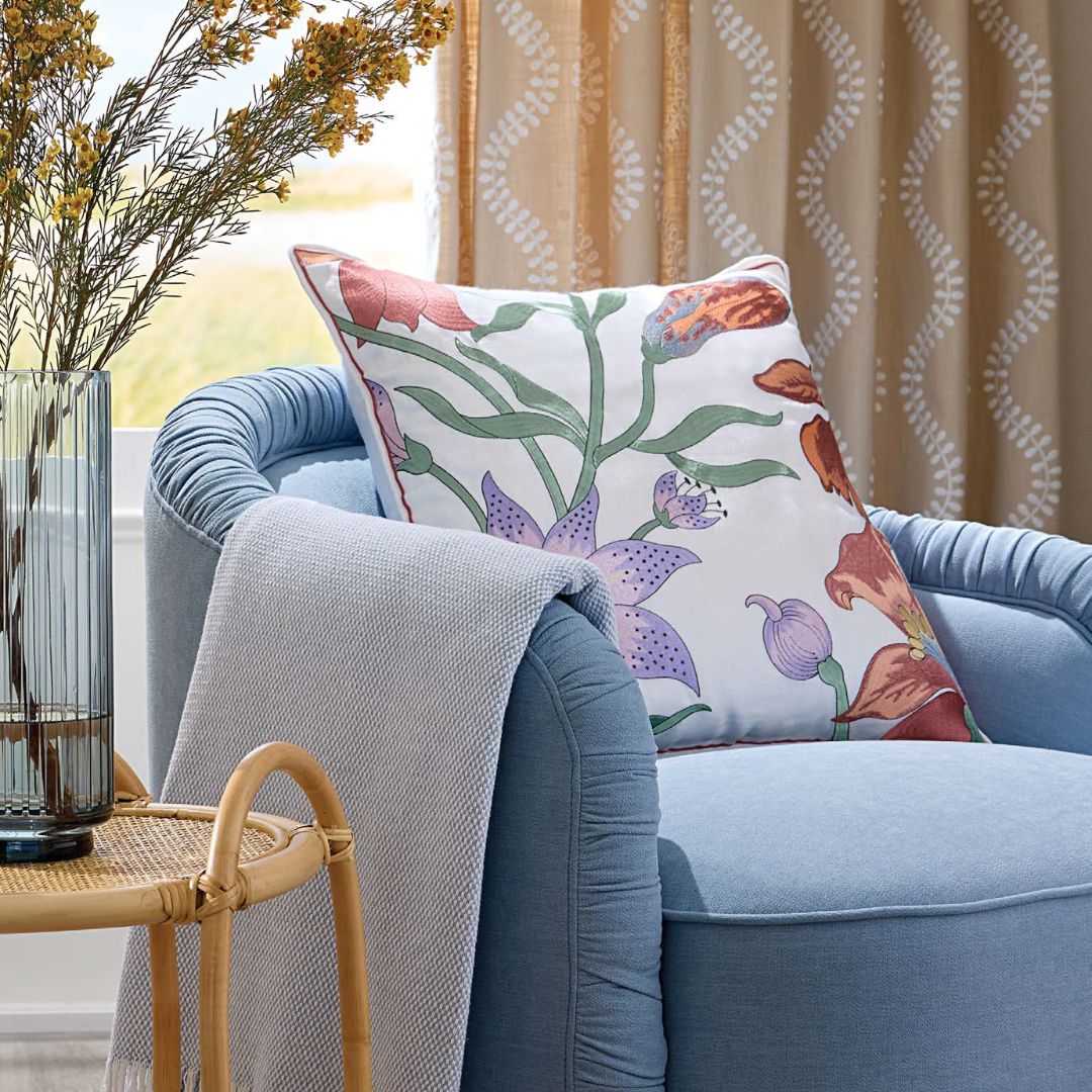 A light blue armchair with a botanical decorative pillow and gray throw blanket next to a table with yellow flowers.