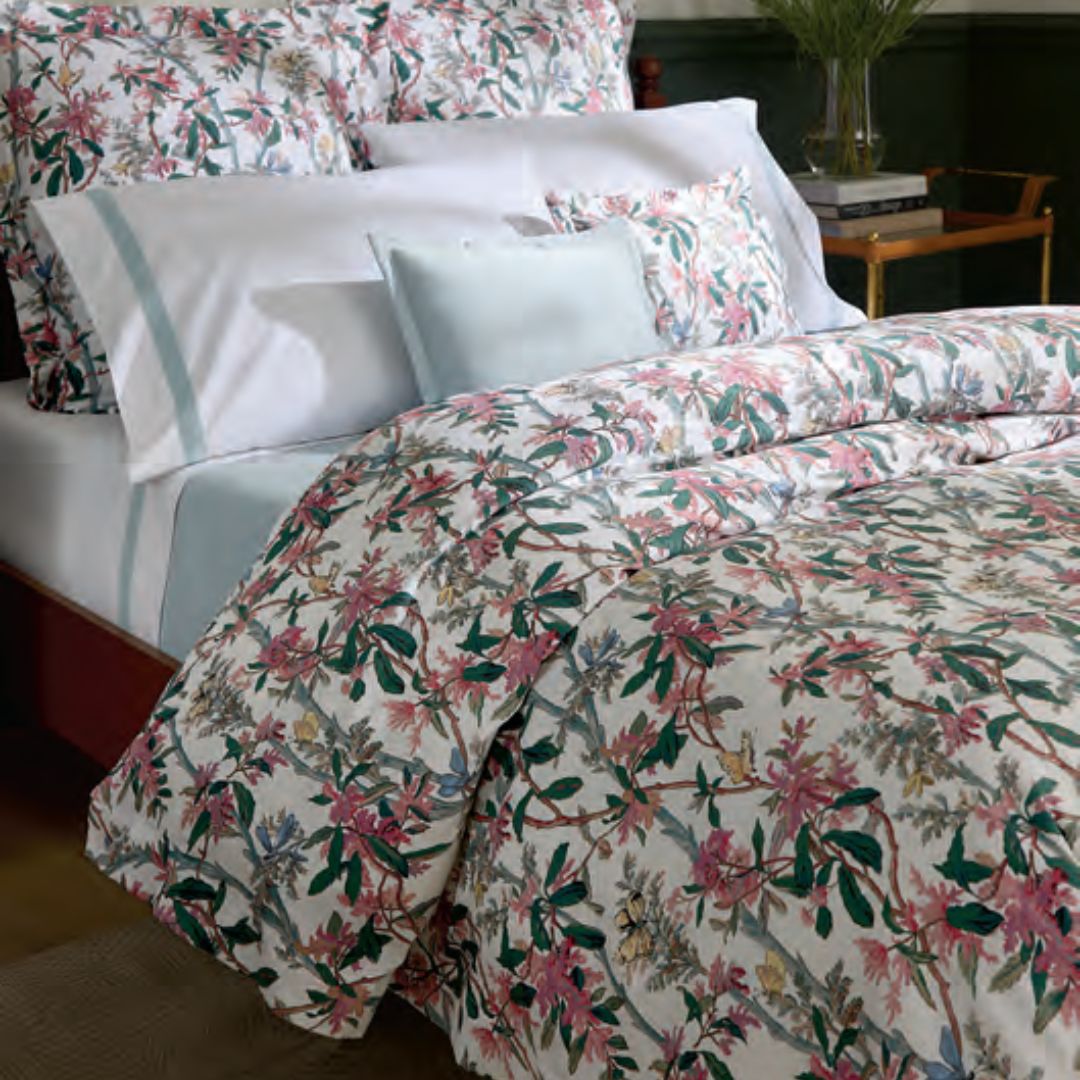 Bed with white and light blue sheets, pillows, and a Sferra Ramaglia Duvet Cover in a botanical garden print.