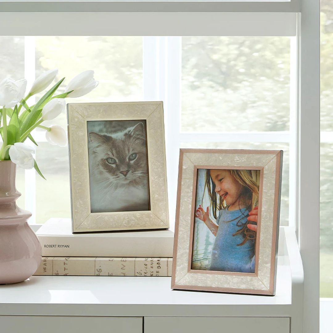 Two framed photos—a cat and a smiling girl—sit on a white table beside handcrafted Italian photo frames and white tulips.
