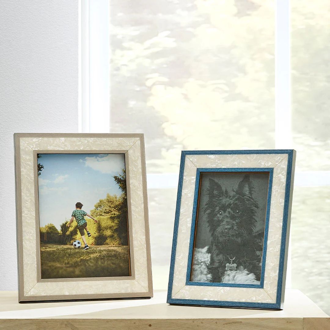 Two framed photos on a wooden surface: one in a handcrafted Italian photo frame, by a window.