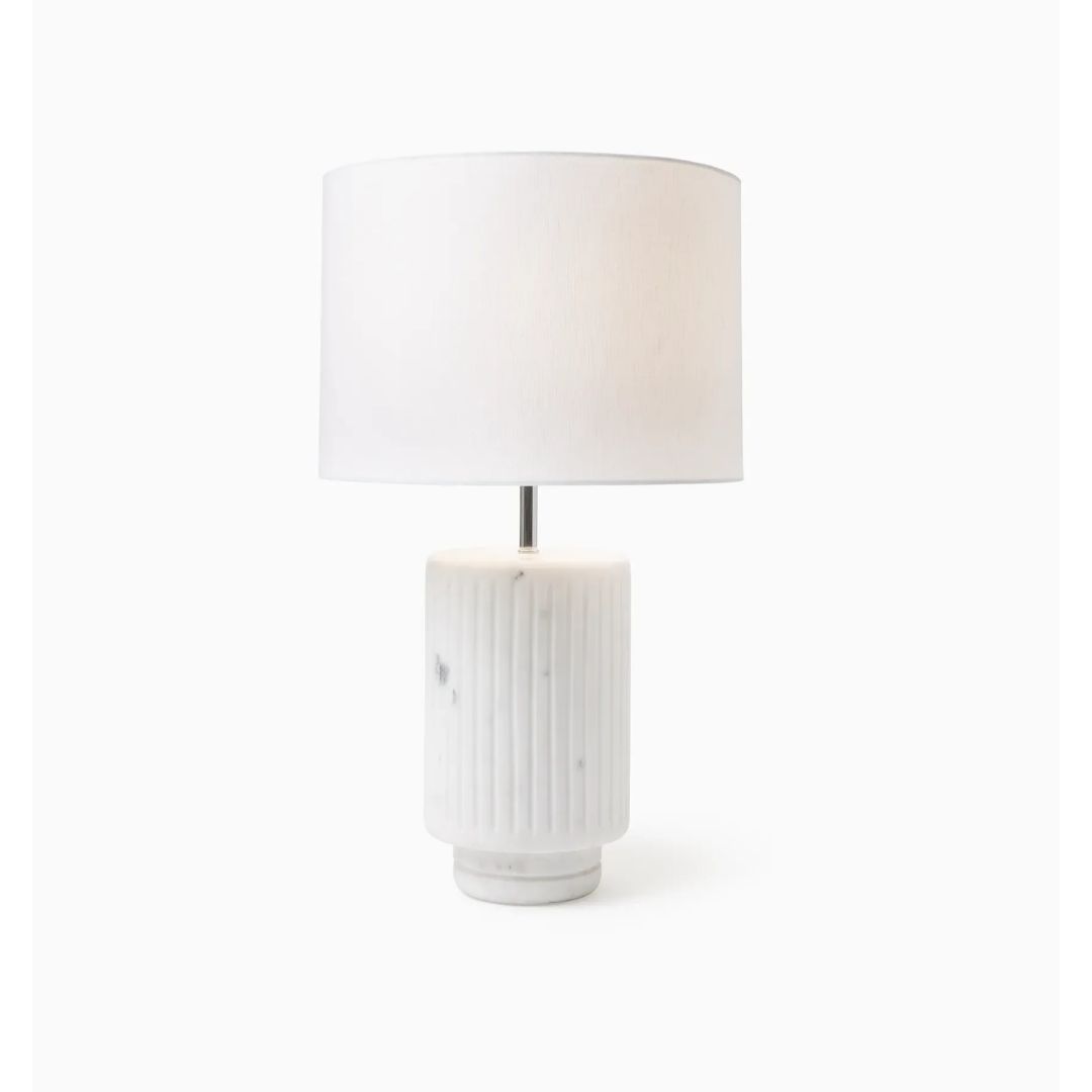 White table lamp with an architectural fluted marble base and a round, white fabric shade on a white background.