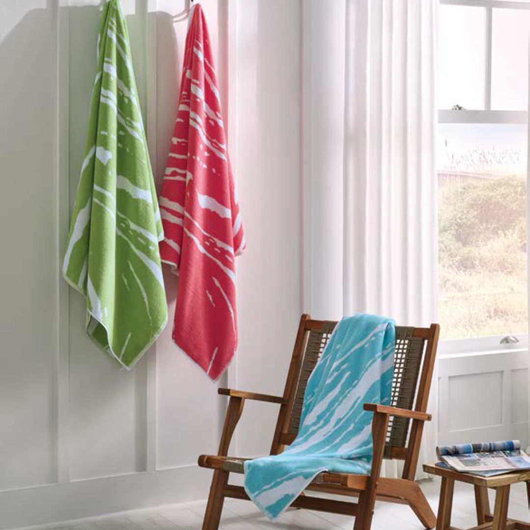 Beach towels in green and pink hanging on wall with a blue beach towel on a chair 
