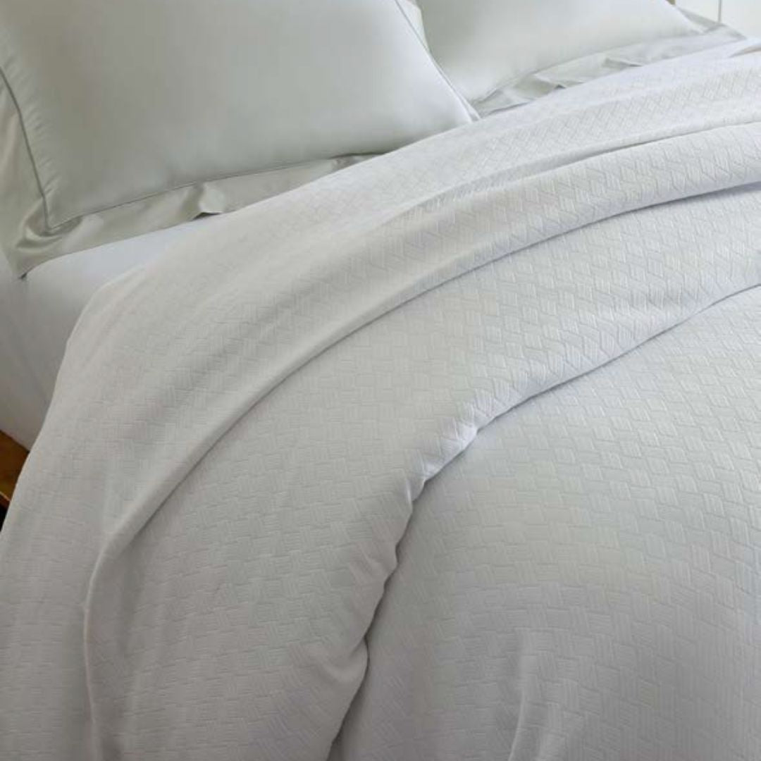 Close-up of a white blanket with a subtle pattern on a bed.