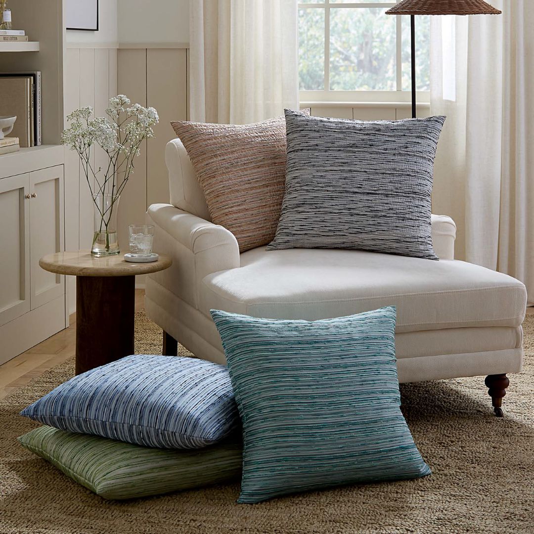 A white chaise lounge with an Italian woven pillow, next to a table with flowers, on a woven rug.