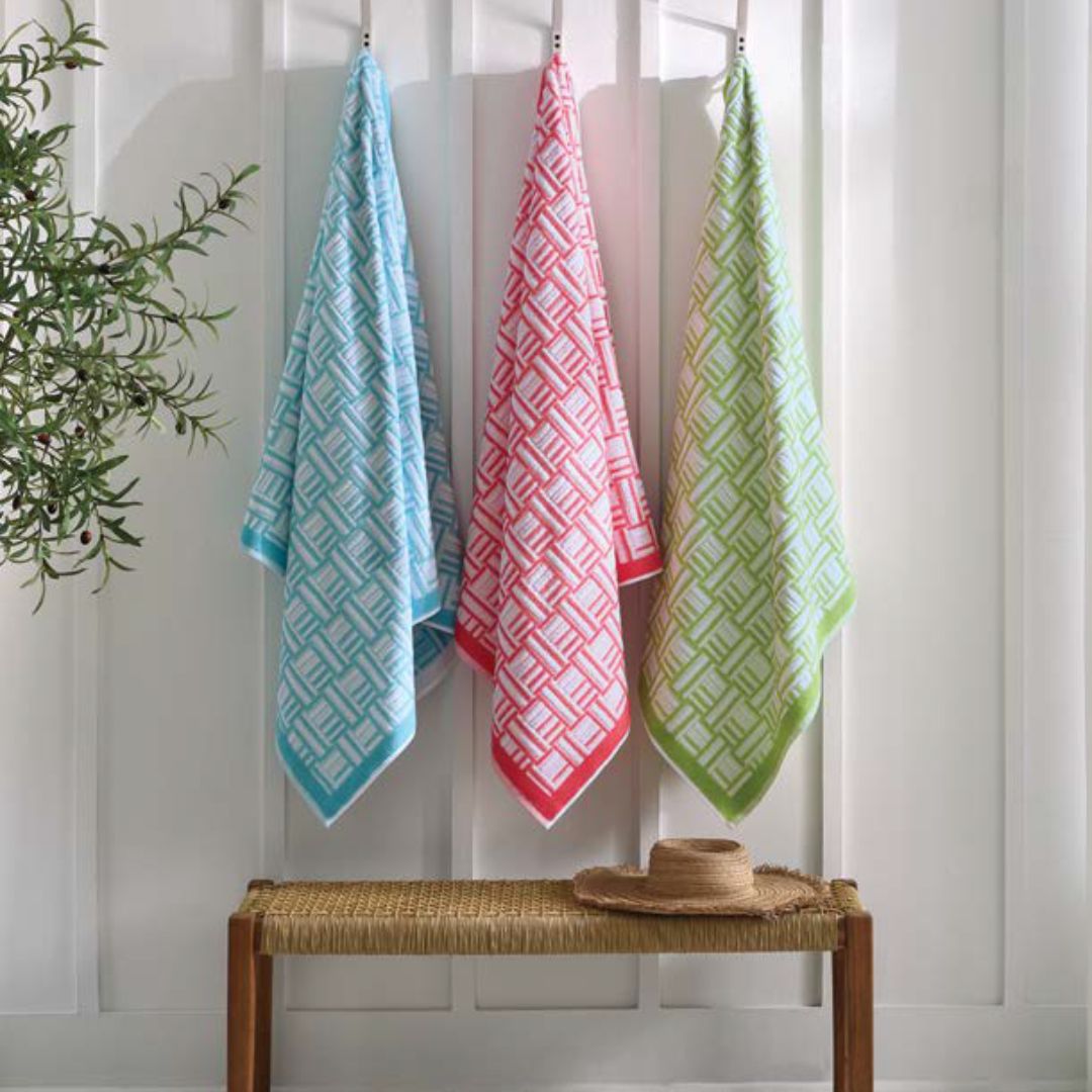 Three Sferra Tirreno Beach Towels with geometric texture hang above a woven bench, adding premium cotton comfort to your space.