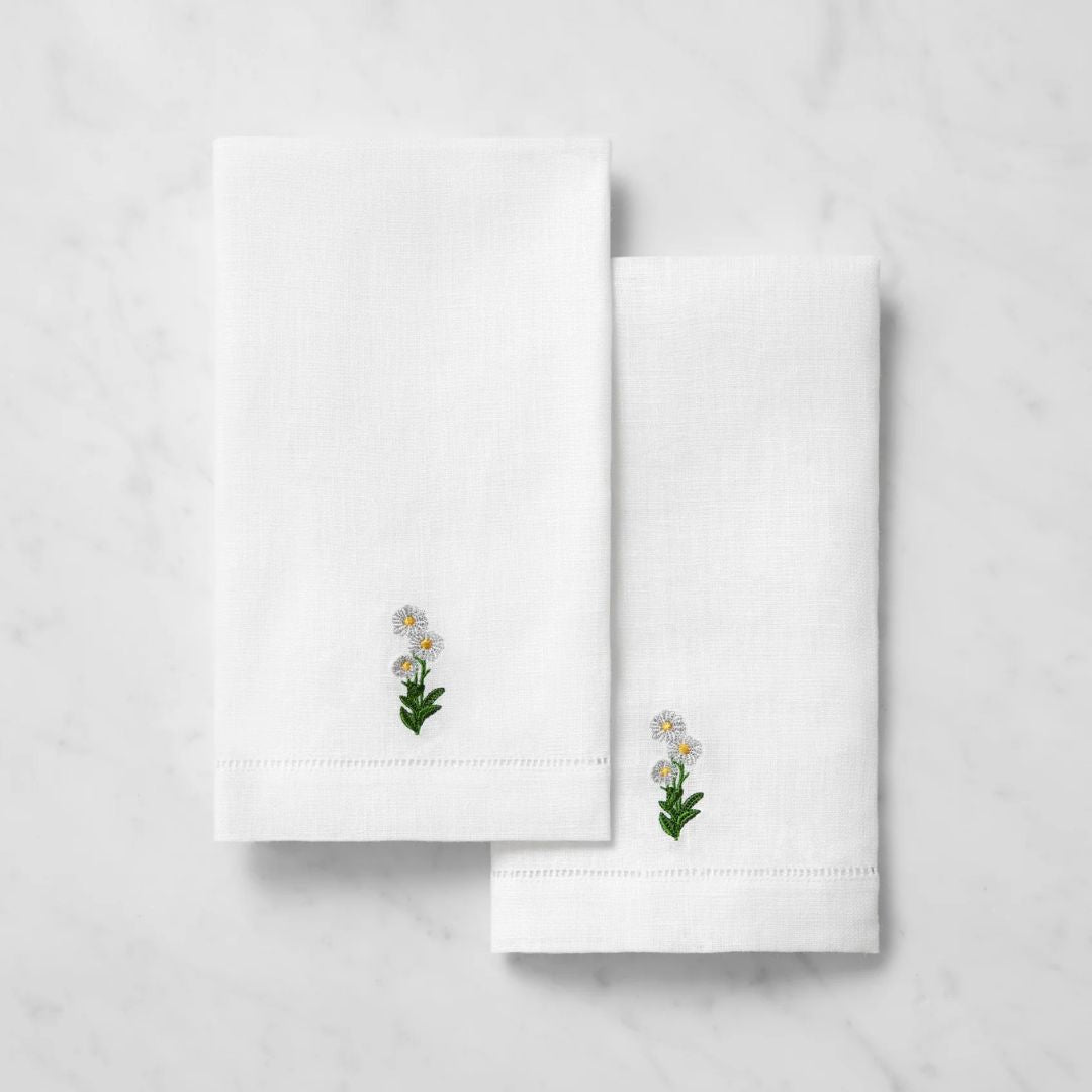 Two Sferra Fiorenza linen guest towels with embroidered white and yellow flowers rest on a marble surface.