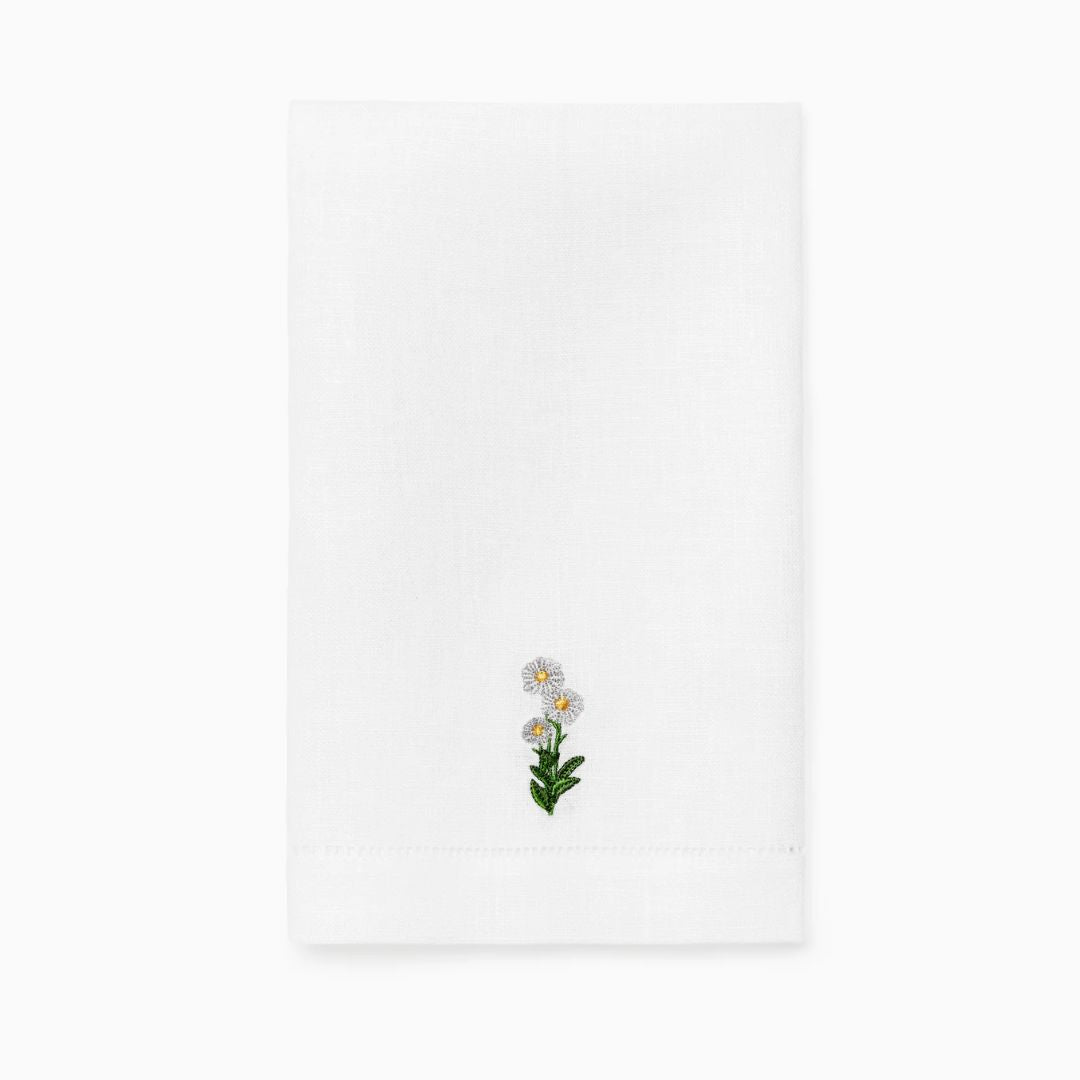 A white linen guest towel with a small embroidered daisy flower and green leaves near the bottom center.
