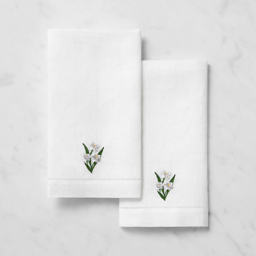 Two white Sferra Fiorenza guest towels with small embroidered flowers and green leaves on a light marble surface.