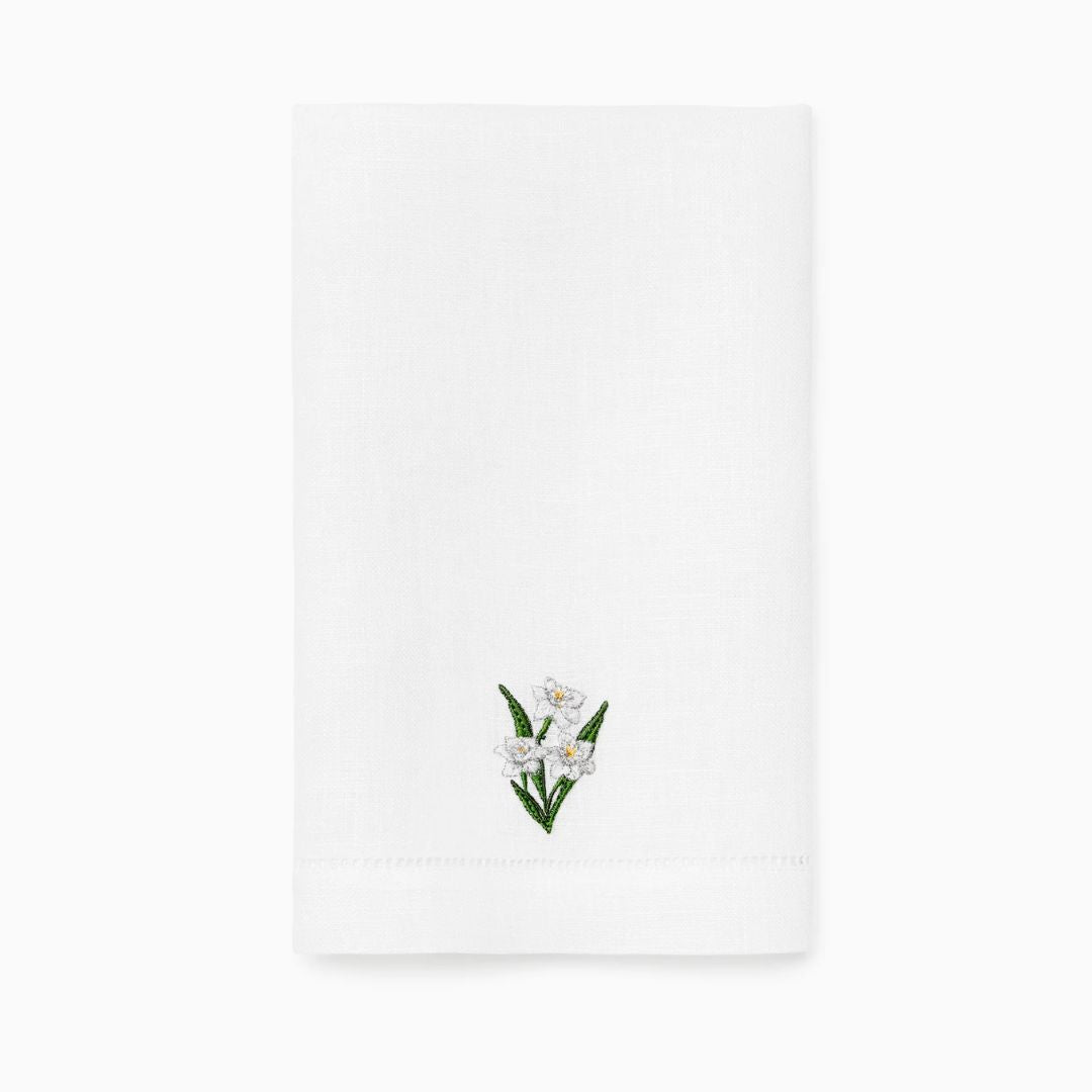 White linen guest towel featuring a delicate embroidered design of white flowers and green leaves near the bottom center.