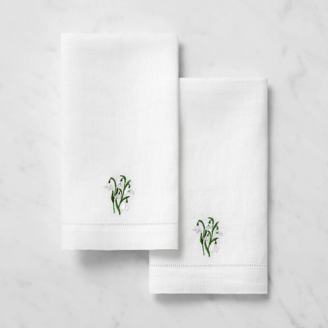 Two white linen guest towels with small green and white flower embroidery, displayed on a marble surface.