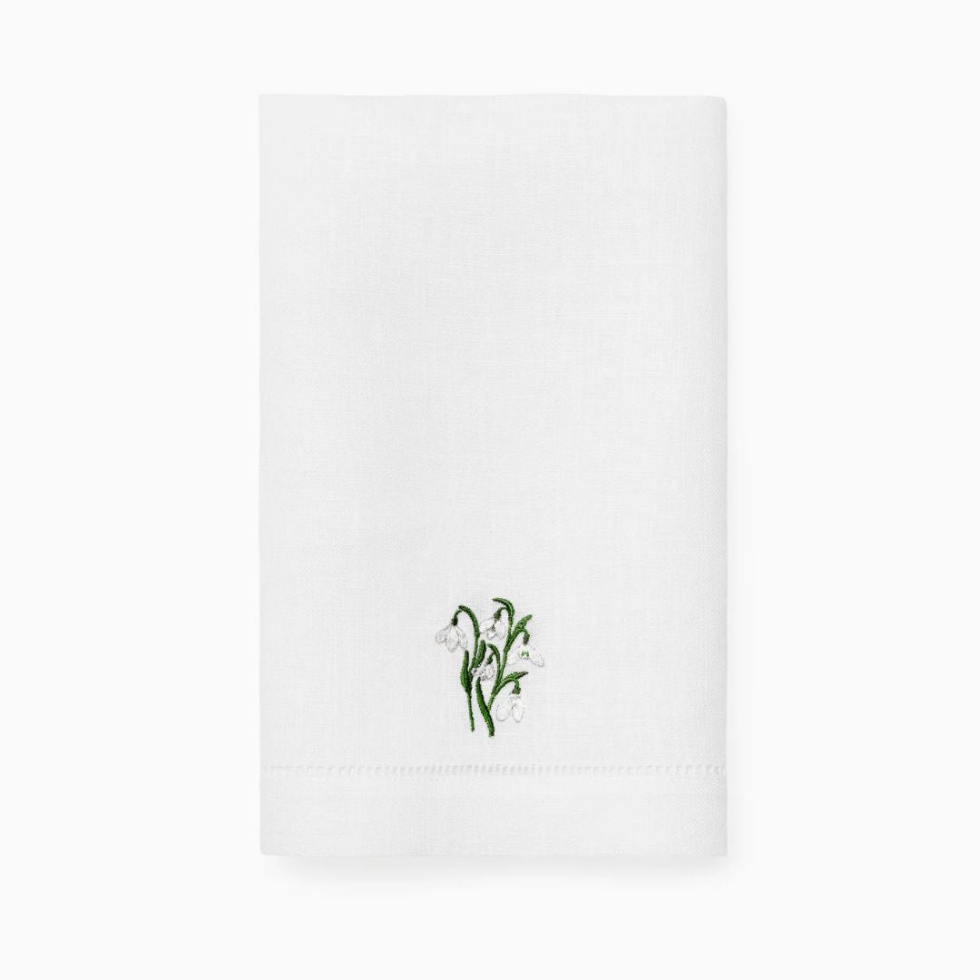 A white folded embroidered guest towel features green leaves and white flowers at the center for a refined touch.