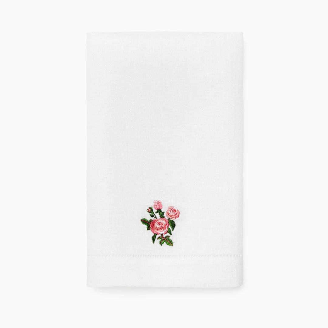 A white linen guest towel with a small embroidered design of pink roses and green leaves near one corner.