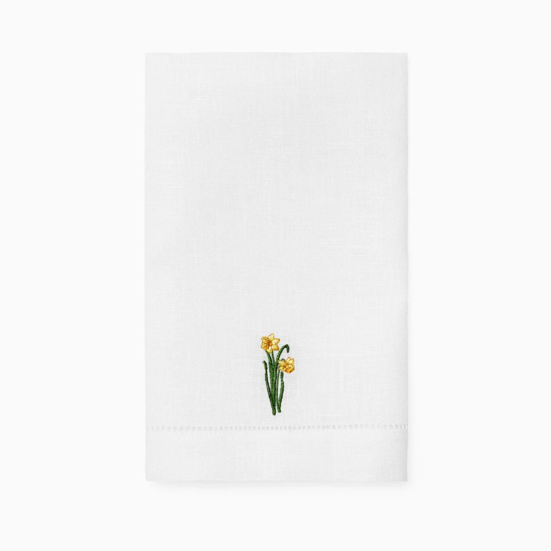White linen guest towel with a small embroidered design of yellow daffodil flowers near the bottom center.