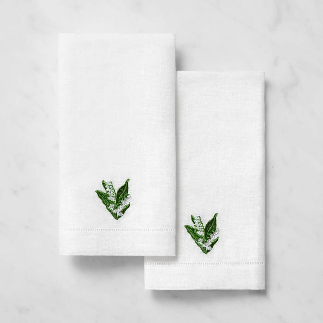 Two white linen guest towels with small green leaf embroidery, placed on a light marble surface.