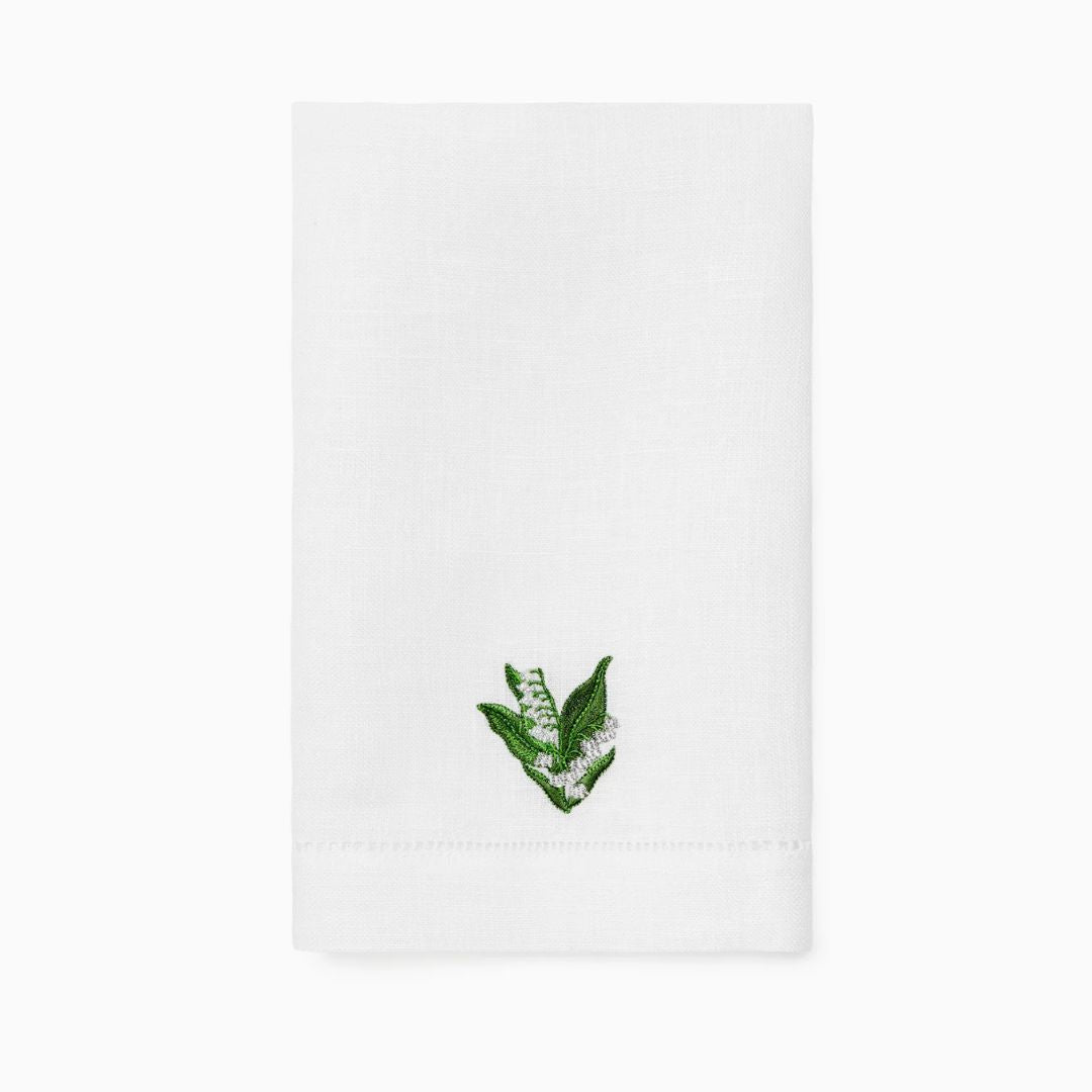 A white linen guest towel with a small green embroidered leaf and white flower design near the bottom center.
