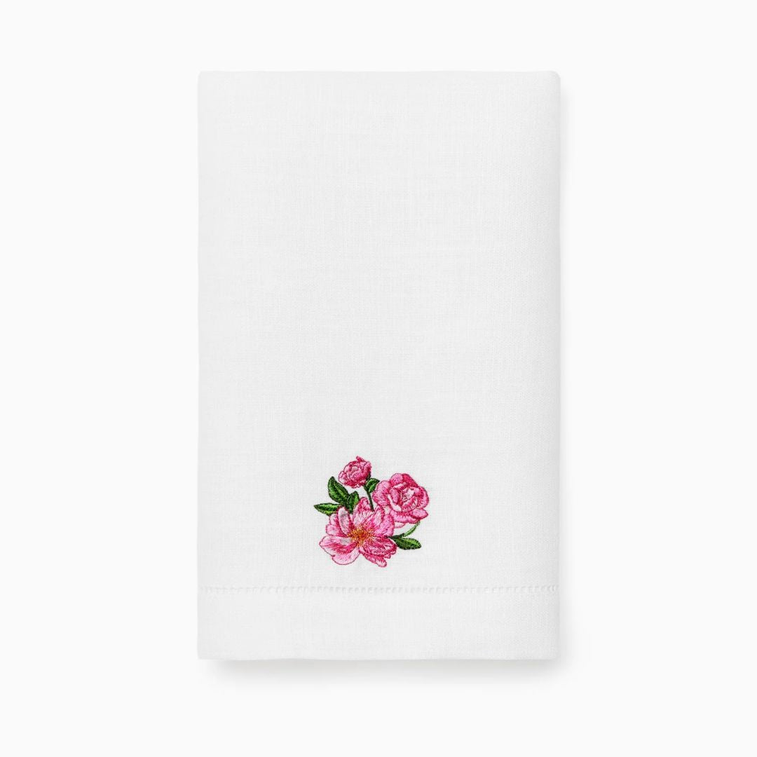 White linen guest towel with a small embroidered cluster of pink roses and green leaves near one corner, folded neatly.