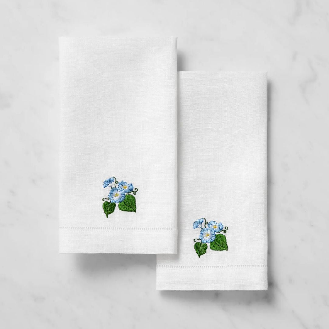 Two white guest towels with floral embroidery on a light gray background
