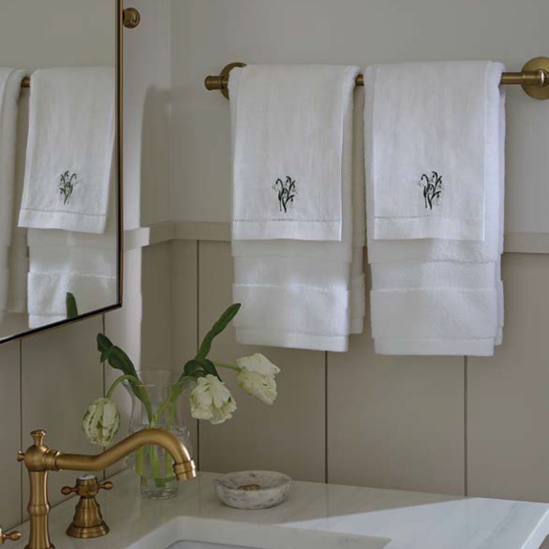Embroidered guest towels hang on a gold towel bar above a sink with a matching gold faucet in the bathroom.