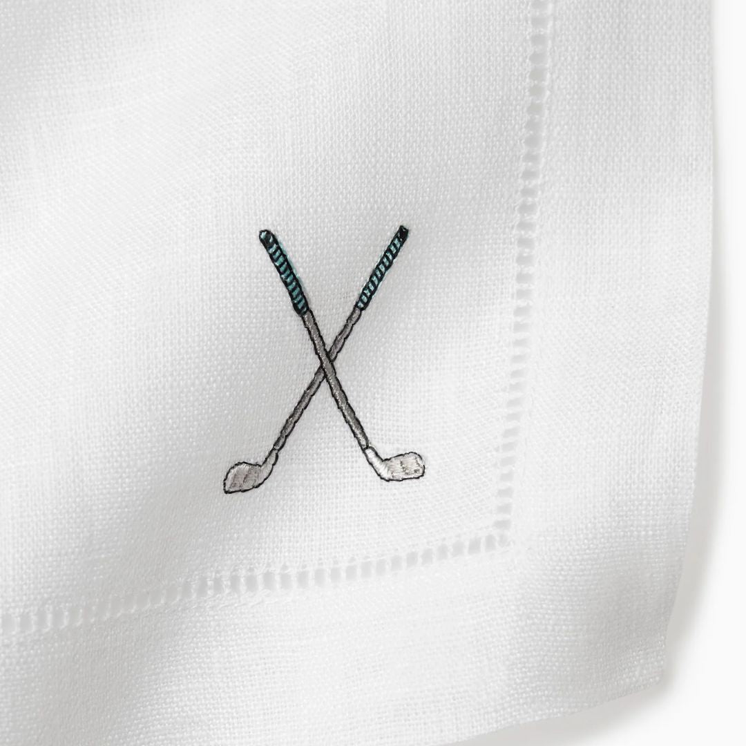 Close-up of a white cocktail napkin with a black embroidered design of two crossed golf clubs.