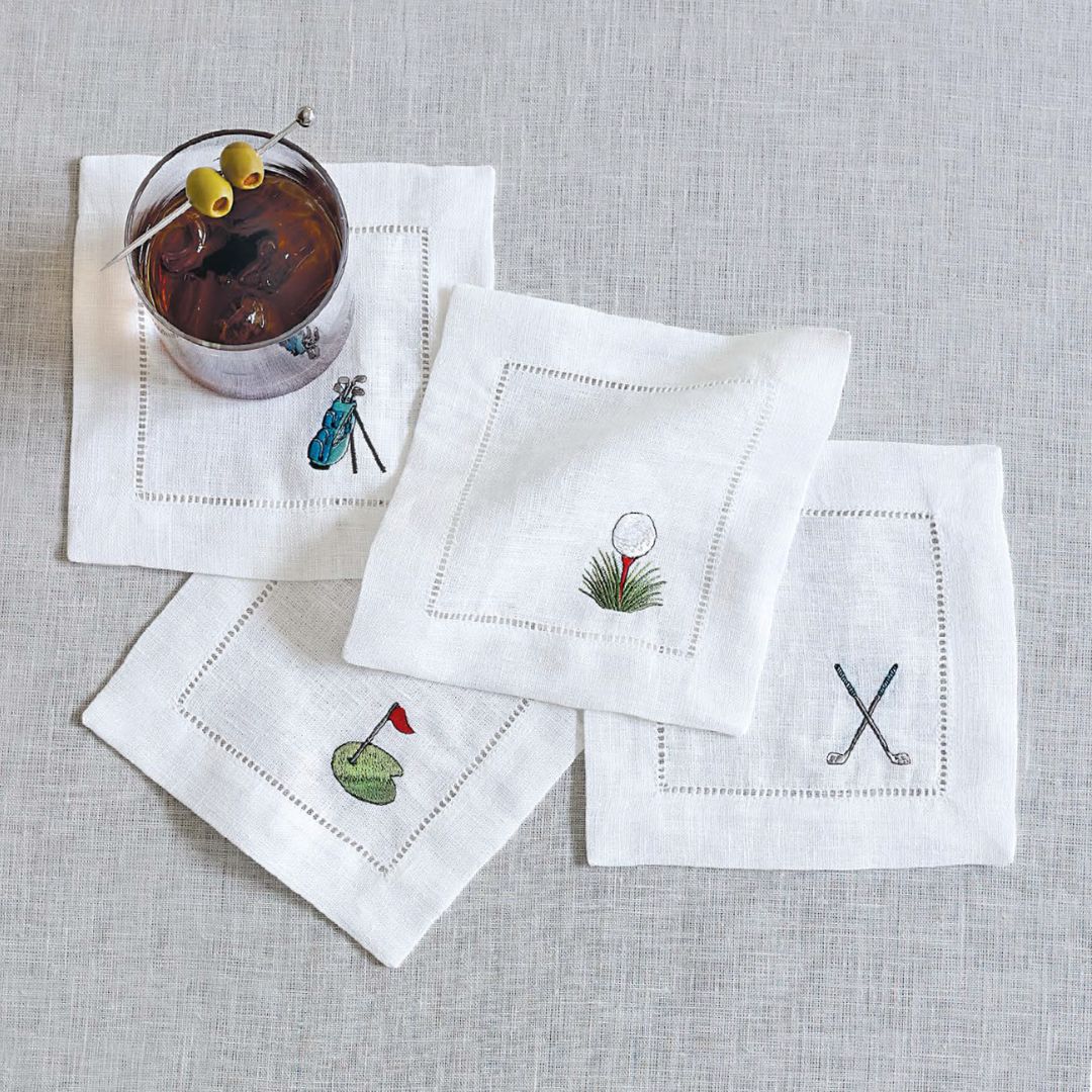 Set of white cocktail napkins with golf-themed designs on a gray surface.
