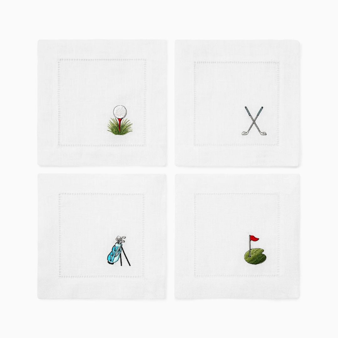Set of four white napkins with golf-themed designs on a white background