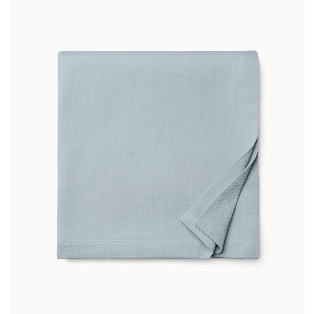A neatly folded light blue Rombo coverlet in cotton matelassé is displayed on a plain white background.