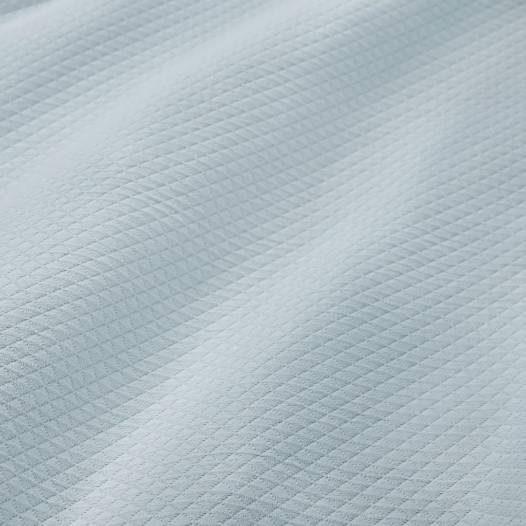 Close-up of a light blue cotton matelassé fabric with a small diamond pattern and gentle waves, from the Rombo coverlet.