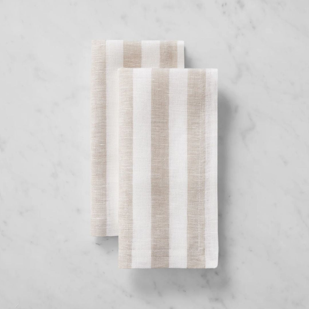 Two folded striped linen table napkins with beige and white stripes, perfect for coastal table decor.