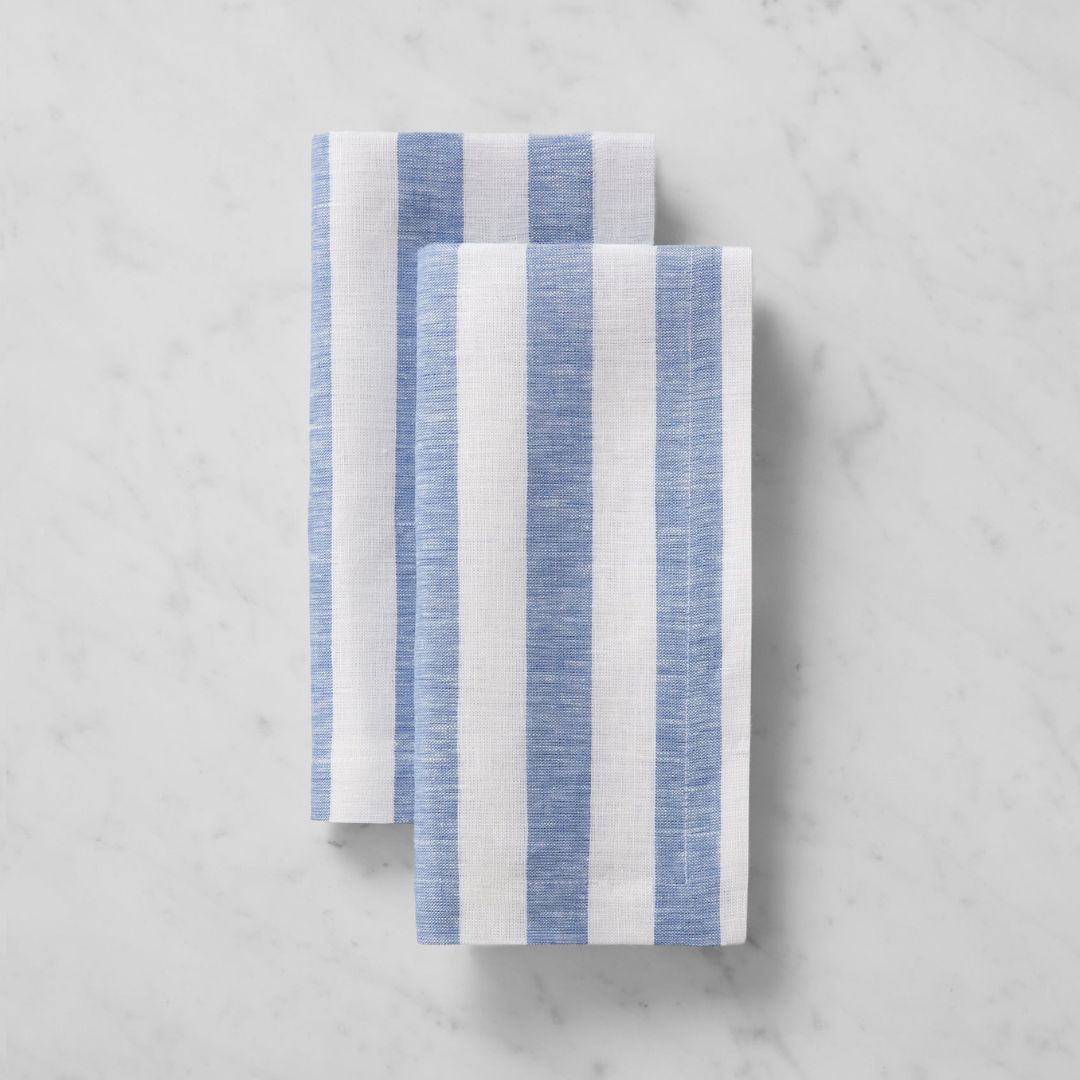 Two folded striped napkins with vertical blue and white stripes, perfect for coastal table decor, on white marble.
