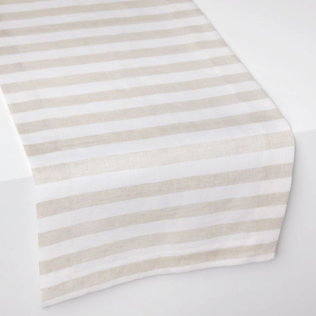 A beige and white striped table runner adds coastal table decor charm to a white surface.