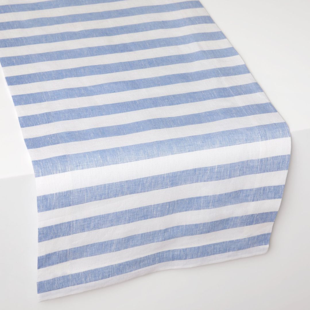 A fabric runner with horizontal blue and white stripes adds coastal table decor to a white surface.