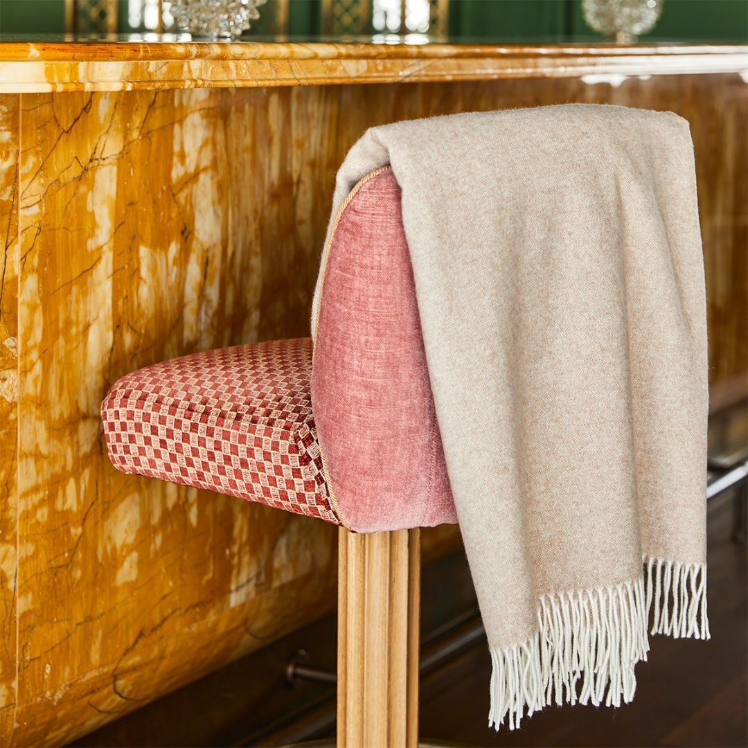 A cream-colored OEKO-TEX certified wool throw draped over a red barstool by a polished, golden marble counter.
